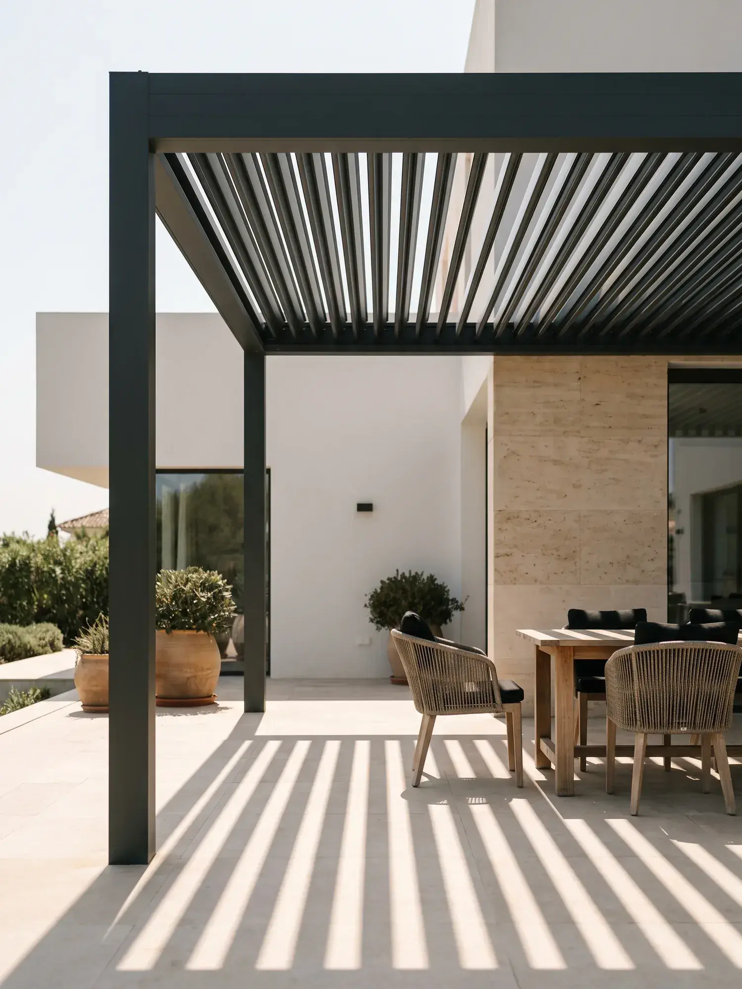 Pergola bioclimatique en aluminium anthracite à lames orientables au-dessus d'une terrasse en pierre